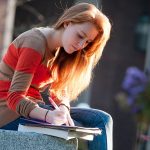 Student sitting on cement wall studying.