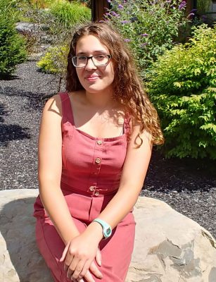 Picture of Jenna Karvelis sitting on a rock, in the sunshine.