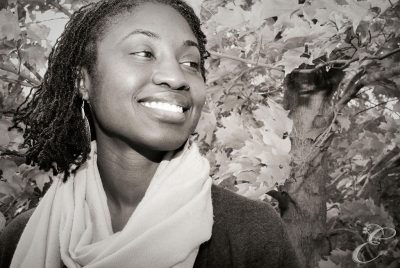 Tricia Hunter, wearing white scarf, standing in front of bushes.