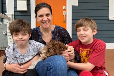 Smiling mother with two sons and their dog, sitting on door step.