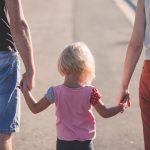 Child holding hands with two adults.