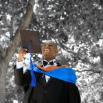 African American male in graduation gown, holding grad cap.