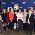 Group of women in front of UConn banner.