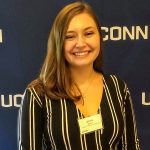 Jenna Racca, Class of 2021 Neag School senior, smiling in front of UConn banner.