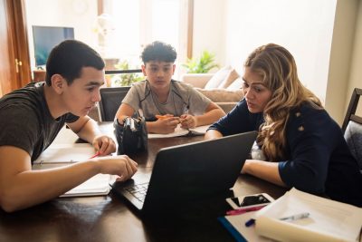 Mother and teenage sons gather around laptop to learn remotely.