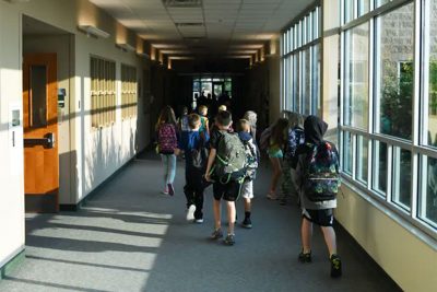 School children walking down hallway, wearing backpacks.
