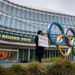 Athlete holds up sign next to Olympic Rings.