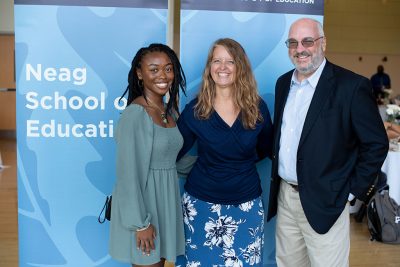 Three adults standing in front of a Neag School banner.