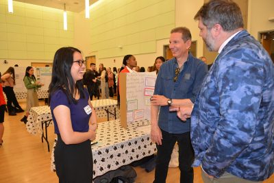 Three people standing and discussing a research poster.